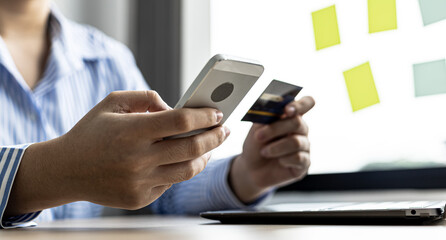 A woman holding a cell phone and credit card, she fills in her credit card information in a mobile shopping app to pay for the purchase. Online shopping concept using credit card payments.