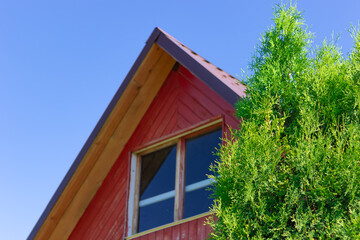 The roof of an old wooden house in a village against a background of blue sky and green foliage. Hot sunny summer day. Selective focus. Close-up