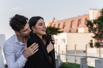 man hugging cheerful woman in black blazer on terrace