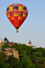 Fototapeta na wymiar A large multicolored hot air balloon flies low over ancient buildings and a tree-lined valley. Photographed at close range