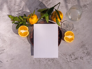 Summer stationery still life. Cut orange fruits on a wooden plate on a white table background in sunlight. Blank white sheet for text. Banquet layout. View from above.