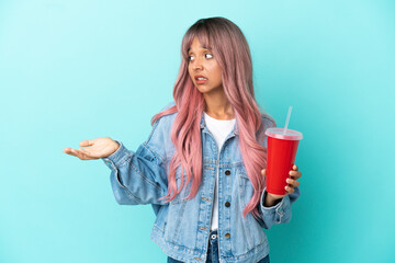 Young mixed race woman drinking a fresh drink isolated on blue background with surprise expression while looking side
