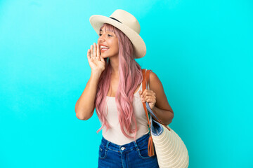 Young mixed race woman holding a beach bag with pamela isolated on blue background shouting with...