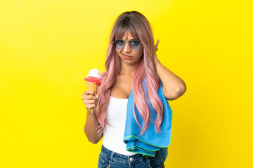 Young mixed race woman with pink hair holding ice cream isolated on yellow background having doubts