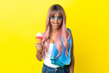 Young mixed race woman with pink hair holding ice cream isolated on yellow background with surprise facial expression