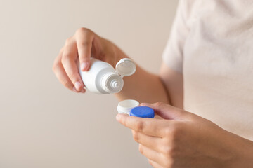 Women's hands with a solution and a container for contact lenses. Close-up. Contact Lens Accessories