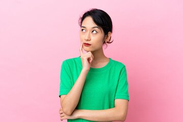 Fototapeta premium Young Vietnamese woman isolated on pink background having doubts while looking up