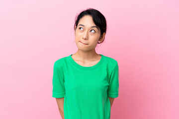 Young Vietnamese woman isolated on pink background and looking up