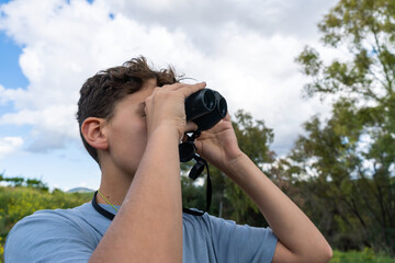 young man in blue shirt observing nature with binoculars