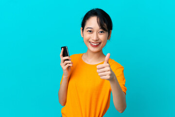 Young Vietnamese woman isolated on blue background using mobile phone while doing thumbs up