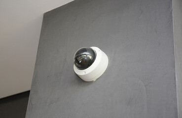 A close-up of a round security camera, security surveillance installed on a gray plastered wall...