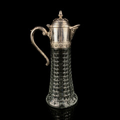 Antique crystal decanter with glass handle and metal neck against black background. Traditional...