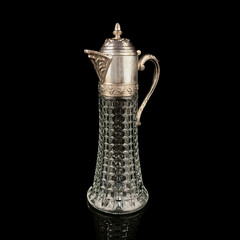 Antique crystal decanter with glass handle and metal neck against black background. Traditional...