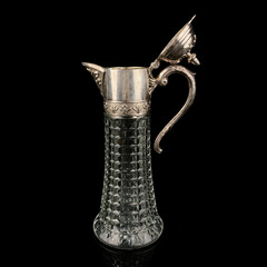 Antique crystal decanter with glass handle and metal neck against black background. Traditional...
