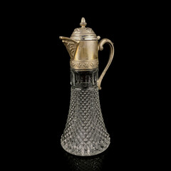 Antique crystal decanter with glass handle and metal neck against black background. Traditional wine jug, Vintage engraving