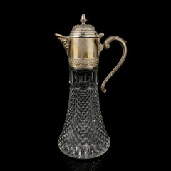 Antique crystal decanter with glass handle and metal neck against black background. Traditional wine jug, Vintage engraving