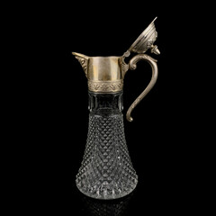 Antique crystal decanter with glass handle and metal neck against black background. Traditional...