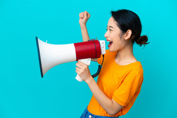 Young Vietnamese woman isolated on blue background shouting through a megaphone to announce...