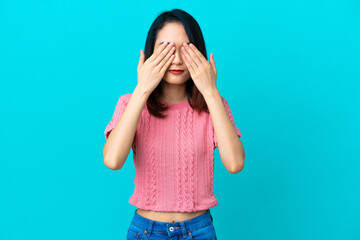 Young Vietnamese woman isolated on blue background covering eyes by hands