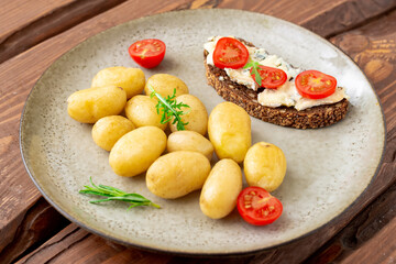 Boiled young potatoes and cereal bread with blue cheese and tomatoes on a plate on a wooden background. Vegetarian food.