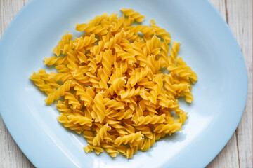 Raw curly pasta on a blue plate on a light wooden background.