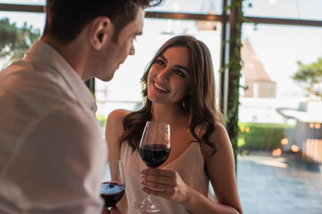cheerful woman holding glass of wine and looking at blurred man