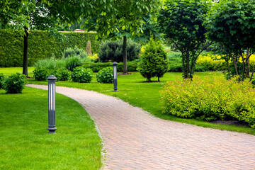 curved pedestrian pavement of stone tiles in park with landscaping and green plants bushes with...