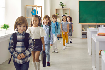 Elementary students leaving classroom. Happy kids entering study room together. Small group of cute little children in casual clothes walking in single file out of classroom after class is over