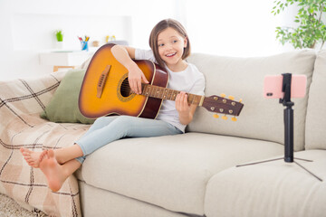 Photo of cute adorable schoolgirl dressed white t-shirt sitting coach playing guitar recording...