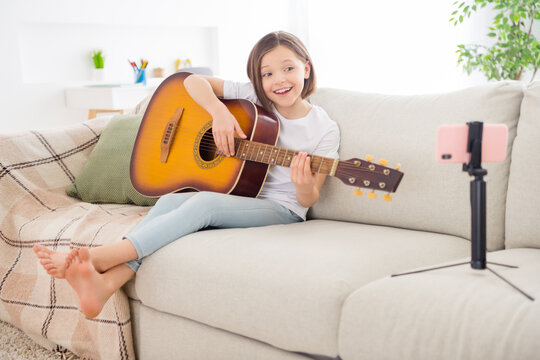 Photo of cute adorable schoolgirl dressed white t-shirt sitting coach playing guitar recording modern gadget indoors room home house