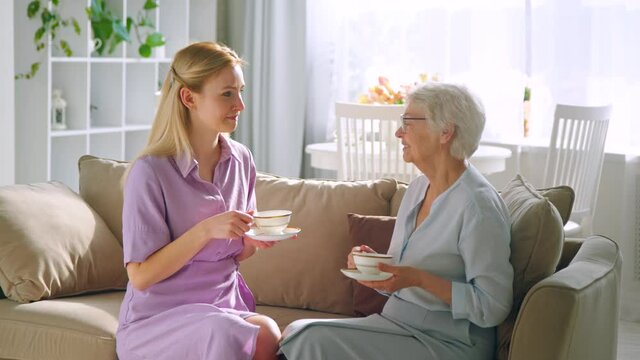Talking smiling daughter and elderly mom with cups of tea
