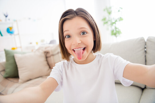 Photo of young cheerful little girl happy positive smile fooling grimace tongue-out make selfie indoors