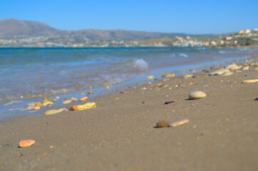 Pebble stones lie on the sandy shore of the blue sea.