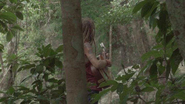 man with dreadlocks playing guitare in the jungle