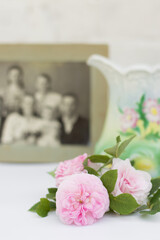 Blurred image of a standing jug, antique photo and roses lying on the table.