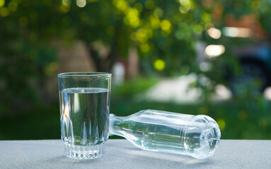 Drinking water bottle and glass against the background of green nature.