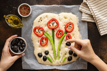 female hands decorating raw focaccia with vegetables and herbs. Italian cuisine, garden focaccia....
