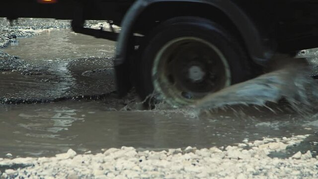 Potholes on the asphalt, road infrastructure damaged after rain. Cars drive slowly along the road with pits and puddles. Asphalt in violation of technology. Taxpayer money is wasted. UHD 4K.