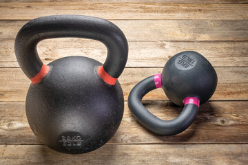 Fototapeta premium two heavy iron kettlebells on a rustic wood background, weight training and fitness concept