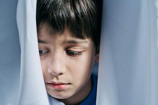 Sad kid looking hiding behind curtains