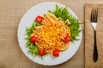 A plate of pasta with cheese and tomatoes decorated with herbs on a wooden table next to a linen napkin and a fork.