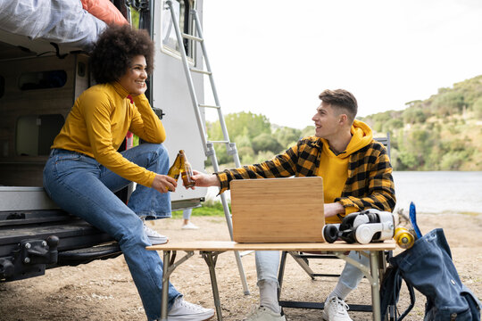 Cheerful diverse couple drinking beer outside van