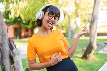 Young brunette woman in the park listening music and doing guitar gesture