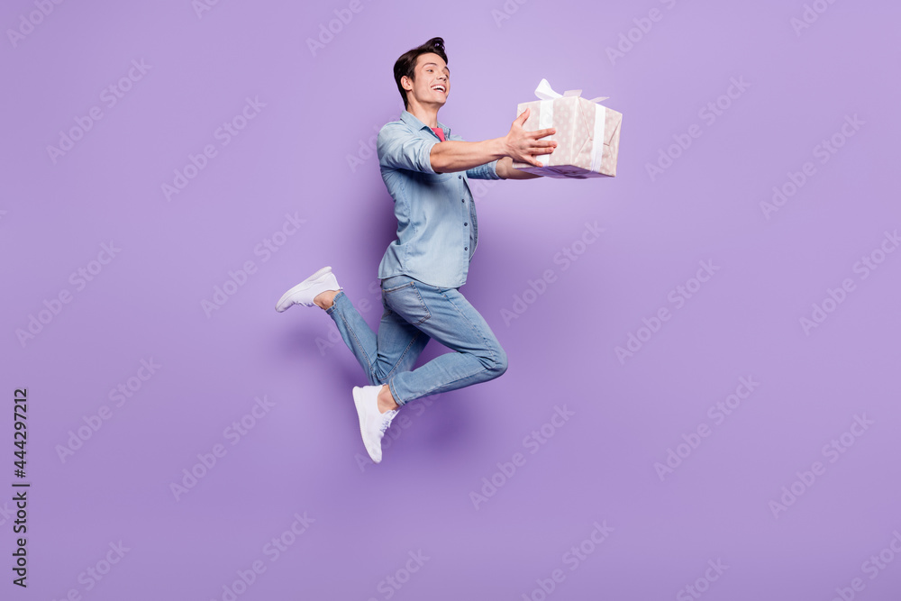 Poster Full body profile side photo of young guy happy smile guest give present box jump isolated over purple color background