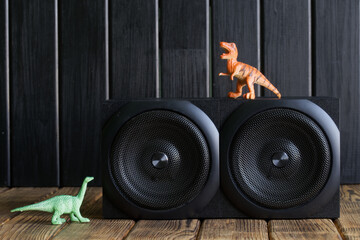 Two-way speaker system next to toy dinosaurs on a background of natural pine boards. An example of...