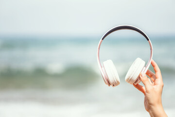 Woman hands with headphones on a beach and sea coastline.