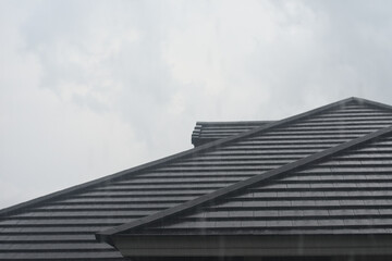 Fototapeta na wymiar Modern dark brown ceramic tile rooftop in stormy sky background. Misty and blurred urban habitat in rainy day atmosphere.