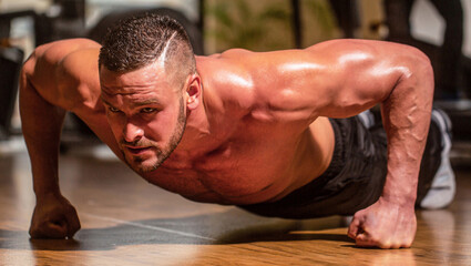Muscular and strong guy exercising. Slim man doing some push ups a the gym. Man doing push-ups. Muscular man doing push-ups on one hand against gym background. Sport