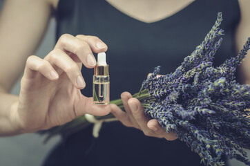 A woman holds lavender oil in her hands. Dropper bottle with lavender oil and fresh lavender flowers in female hands