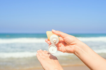 Woman applying sunscreen on skin of hand on a beach of coastline sea. Female relaxation at summer vacation. Back view